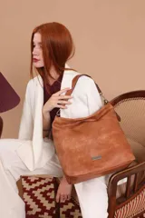 Cartera tipo bandolera de gran tamaño, confeccionada en cuero sintético con acabado desgastado. Cuenta con una asa corta fija, una correa larga regulable y extraíble, y una placa metálica con la marca en la parte frontal.