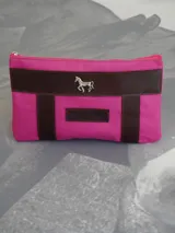 Sobre tipo cartuchera de lona naranja con detalles y apliques en cuero marrón. Presenta un aplique metálico en forma de caballo y un parche con el logo de la marca grabado en el frente.