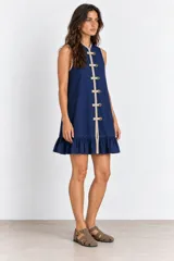 Vestido corto azul marino sin mangas, con cuello mao y cierre frontal de alamares decorativos en tono beige. Presenta ribetes en contraste y un delicado volado en el ruedo.