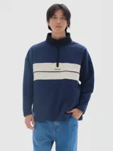 Buzo de felpa azul marino con interior de friza, cuello alto negro y media cartera con cierre. Presenta un corte horizontal en el pecho en color beige con el logo "PASTICHE" bordado en negro.