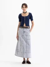 Pollera midi de denim en color azul claro con efecto lavado. Presenta un diseño de corte recto con costuras decorativas visibles, bolsillos frontales tipo cargo y una abertura central en el ruedo.