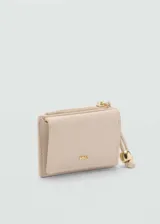 Monedero compacto de efecto piel en color beige, con cierre de solapa magnética y bolsillo lateral con cremallera. Incluye un detalle decorativo de cordón con abalorios metálicos y el logo de la marca grabado en el frente.