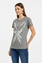 Remera negra de manga corta, con cuello redondo y ajuste al cuerpo. Cuenta con un gran estampado floral en tono gris en el frente y detalle de tachas plateadas alrededor del cuello y en los puños.