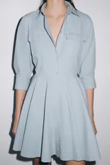 Vestido corto tipo camisero de algodón, con cuello solapa, mangas tres cuartos y cierre frontal con botones. Presenta bolsillos de plastrón con solapa en el pecho y falda con bajo plisado.