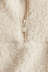 Buzo de corte oversized confeccionado en tejido de sherpa suave. Presenta cuello elevado con medio cierre frontal, hombros caídos y bolsillos insertados en el frente. Incluye canesú en la parte delantera y trasera.