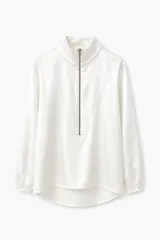 Blusa de satén color blanco con cuello alto y cierre frontal parcial. Presenta mangas largas con puños elásticos y un diseño de corte fluido con ruedo redondeado.