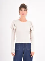 Remera de manga larga en color beige, confeccionada en tejido acanalado, con cuello redondo y detalle de volados en los hombros.
