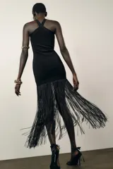 Vestido largo negro de tejido elástico, con escote halter y bajo con flecos a tono.