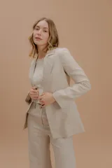 Blazer de lino color beige, de corte estructurado con solapas clásicas, cierre frontal y bolsillos laterales con solapa.