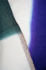 Bufanda tipo manta multicolor con diseño en bloques de color (blanco, verde oscuro y azul) y flecos en los extremos.