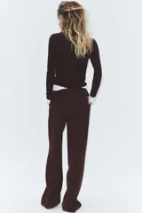 Pantalón negro de tiro alto, con trabillas, bolsillos laterales y de vivo en la espalda. Presenta pliegues en el delantero y cierre frontal con botón.