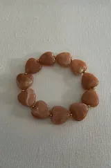 Pulsera elástica compuesta por cuentas de acrílico en forma de corazón color rosa tierra con efecto marmolado, intercaladas con pequeñas cuentas esféricas de acero dorado.