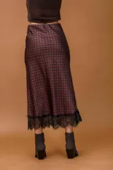 Falda midi de seda con estampado de lunares rojos sobre fondo oscuro, con detalle de encaje negro en el ruedo.