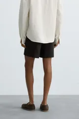 Bermuda de corte relajado confeccionada en tejido de lino color gris oscuro. Presenta cintura elástica con cordón de ajuste interno, bolsillos laterales y bolsillos traseros de plastrón.