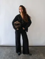 Camisa de denim negro con cuello en V, cierre frontal con botones metálicos y dos bolsillos cuadrados en el frente. Presenta un corte recto y oversize con ajuste en la espalda.