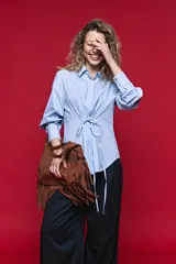 Camisa blanca de manga larga con volumen y estructura, cierre frontal con botones y lazo ajustable en la cintura que realza la silueta.