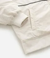 Campera bomber de microfibra color beige con estampado frontal de lettering 'PARIS 1985'. Presenta cierre frontal con cremallera, cuello alto, bolsillos funcionales y puños y ruedo ajustados con elástico.