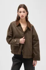 Campera de estilo encerado color marrón, con cuello de pana en tono contrastante, cierre frontal con cremallera y botones a presión, y bolsillos laterales. Presenta un diseño holgado con forro interior a cuadros.