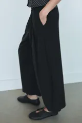 Pantalón fluido de tiro medio color verde militar, con cintura elástica en la parte trasera, pinzas en el delantero y bolsillos laterales ocultos en la costura. Presenta un diseño de pernera ancha y corte tobillero, con cierre frontal de cremallera y botón.