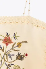 Top color crudo con tirantes finos y escote recto. Presenta bordado floral en el frente y detalle de encaje en el ruedo y escote.
