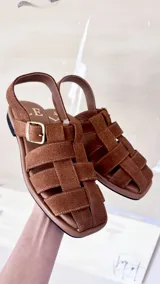 Sandalias de cuero negro con diseño de tiras entrelazadas, estilo huarache, con pulsera ajustable al tobillo mediante hebilla metálica.