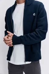 Cardigan de punto color azul marino, con cierre frontal completo, cuello alto y puños acanalados. Presenta un pequeño bordado distintivo en el pecho.