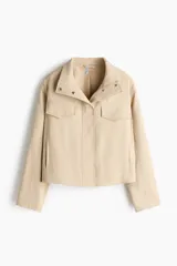 Campera beige con cuello chimenea, botones a presión ocultos en la parte delantera, bolsillos superiores con solapa y bolsillos laterales. Cuenta con diseño forrado y ajuste con cordón elástico en el bajo.