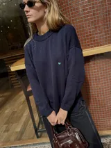 Buzo de punto color azul marino con diseño de conejos bordados a mano en la espalda en tonos rojizos y detalles de puntos verdes en el ruedo. Presenta cuello redondo y mangas largas.