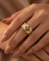 Anillo ancho de bronce con baño de oro y acabado texturizado, decorado con un diseño central geométrico de circonias incrustadas y detalles en los extremos.