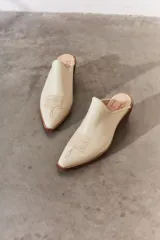 Mule de cuero color suela con diseño de punta fina y bordado decorativo en el empeine. Presenta un taco bajo de madera y una silueta abierta en el talón.