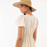 Vestido corto de corte evasé, con estampado floral sutil en tonos rosados y verdes sobre base blanca. Presenta escote en V y mangas cortas tipo mariposa.