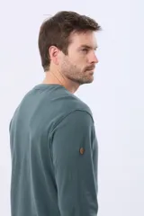 Remera de algodón texturada color gris oscuro, de manga larga, con cuello redondo y botones en la parte frontal. Presenta un pequeño logo bordado en el pecho y un parche decorativo en la manga izquierda.