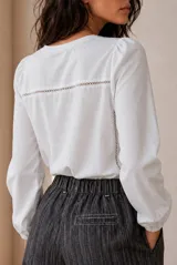 Remera blanca de manga larga con detalles de encaje en el frente y puños elásticos.