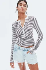 Remera ajustada de punto acanalado, color blanco con rayas finas bordó. Tiene cuello redondo con ribete de picot y tapeta de botones en la parte delantera.