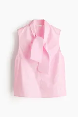 Blusa sin mangas color rosa claro, con cuello alto y lazo ancho anudado al frente. La tela principal es lisa, mientras que el lazo presenta una textura de líneas finas verticales.