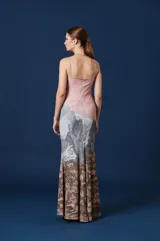 Vestido largo de corte ajustado con breteles finos y escote recto. Presenta un diseño estampado que combina un fondo rosado en la parte superior con una ilustración paisajística de montañas, bosques y ciervos en tonos grises y marrones en la parte inferior.