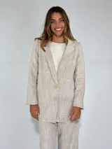 Blazer de lino y algodón en tono beige con textura a rayas verticales sutiles. Presenta solapas clásicas, un solo botón frontal marrón y un corte ligeramente holgado. Los bordes de las mangas y el ruedo tienen un acabado deshilachado.