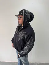 Campera reversible con cierre frontal, diseño oversize. Un lado es de algodón negro con estampados y bordados gráficos, mientras que el otro lado es de tela polar gris de pelo largo. Cuenta con capucha, puños y ruedo acanalados.