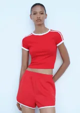 Short deportivo de corte recto, color rojo con ribetes blancos en contraste en los bordes inferiores. Cuenta con cintura elástica y bolsillos laterales.
