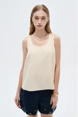 Musculosa de viscosa color beige claro, holgada, con cuello redondo y tirantes anchos formados por múltiples tiritas trenzadas.