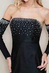 Vestido largo de fiesta color negro, con diseño strapless y ajuste al cuerpo. Presenta un detalle de pedrería brillante en la parte superior del busto y una falda con caída fluida.