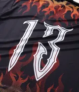 Remera de manga larga con corte boxy, confeccionada en microfibra de poliéster. Presenta un diseño estampado con motivos de llamas en tonos rojos y naranjas, junto con el número 13 en tipografía gótica en la espalda.