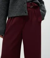 Pantalón de corte wide leg confeccionado en crepé color bordó, con cintura alta, cierre frontal con cremallera y detalle de hebilla ajustable en la cintura.