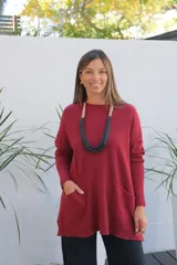 Sweater de punto color bordó, con cuello redondo, mangas largas y bolsillos frontales tipo parche. Presenta un corte holgado y diseño asimétrico con terminaciones en rib.