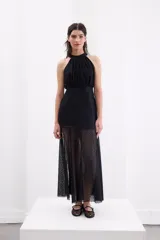 Vestido largo de encaje negro, con escote halter y falda translúcida con tajo delantero.