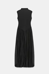 Vestido largo sin mangas con cuello subido, confeccionado con una parte superior lisa y falda de tul con caída fluida. Cuenta con cierre de cremallera oculta en la espalda.