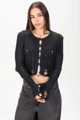 Cardigan corto de tejido de punto acanalado en color negro, con mangas largas y detalles desgastados o rotos en el frente y puños. Cierre frontal con pequeños botones redondos.