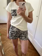 Conjunto de pijama de dos piezas, compuesto por una remera color crema de manga corta con bolsillo en el pecho y un short con estampado animal print de cebra en blanco y negro.