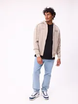 Canguro gris con capucha, cierre frontal completo y bolsillos tipo canguro. Presenta detalles de líneas blancas en las mangas y estampados gráficos en el pecho.