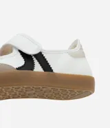Championes estilo chutera de mujer, con diseño de punta redonda y cierre de velcro. Presenta una combinación de colores blanco, beige y negro con recortes contrastantes y suela plana color caramelo.